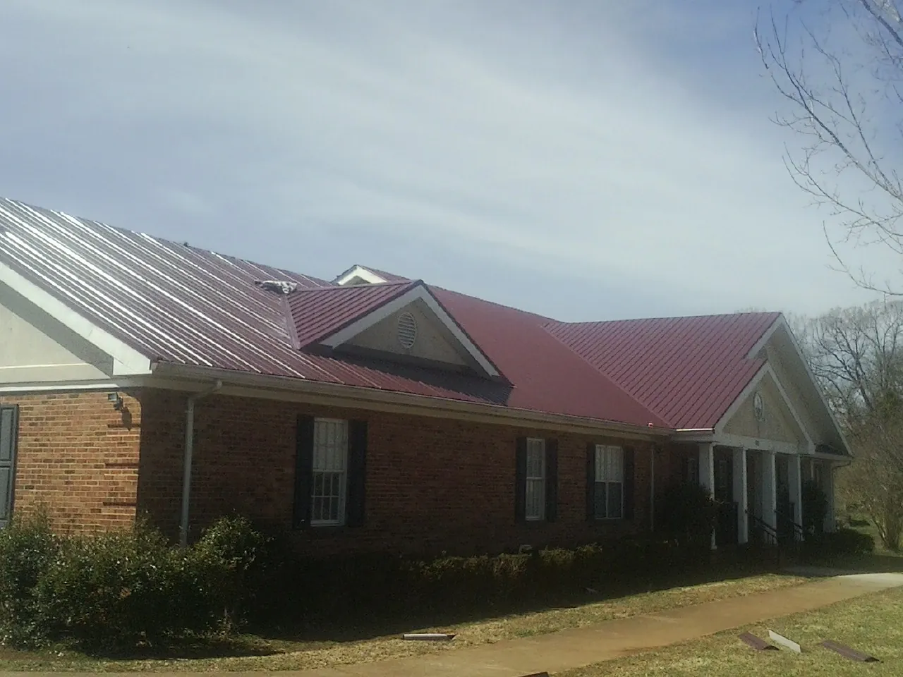 Red metal roof with gabled entries on a long brick building, from a Hail Damage Roof Repair job in Deptford