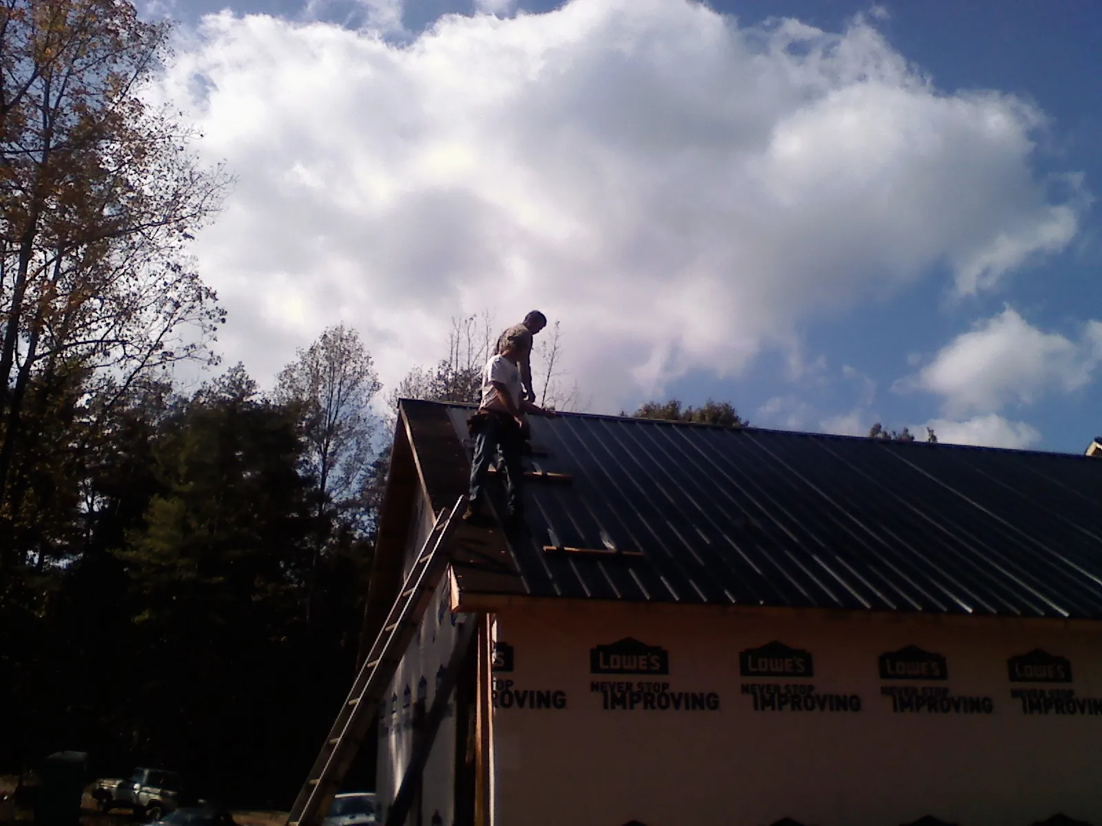 Roofer fastening dark metal panels high against a cloudy sky, from a Roof Inspection job in Deptford