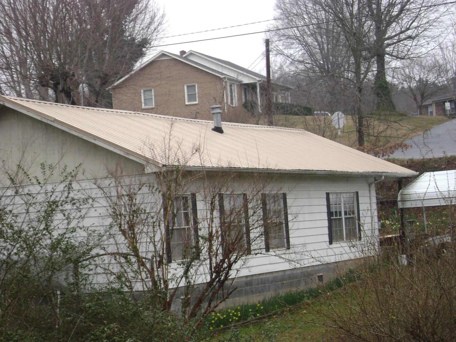 Tan metal roof on a white sided house set into a hillside — Commercial Roofing by Roofing Brothers in Deptford